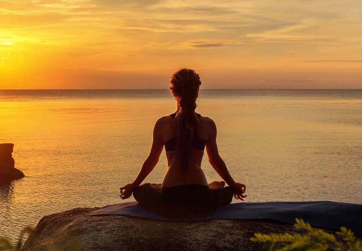A person sitting peacefully in meditation overlooking a calm lake